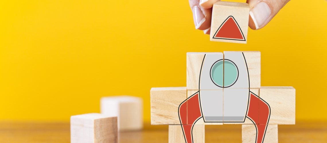Hand arranging wooden cubes in a structure rocket shape. Conceptual of business startup and strategy.