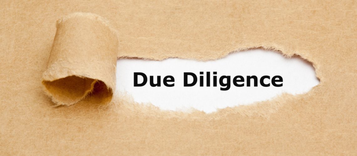 Text Due Diligence appearing behind torn paper. Concept representing the research done before entering into an agreement or contract as a part of the risk analysis process.