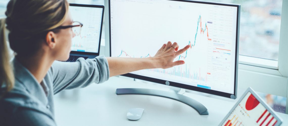 Business woman study financial market to calculate possible risks and profits.Female economist accounting money with statistics graphs pointing on screen of computer at desktop. Quotations on exchange