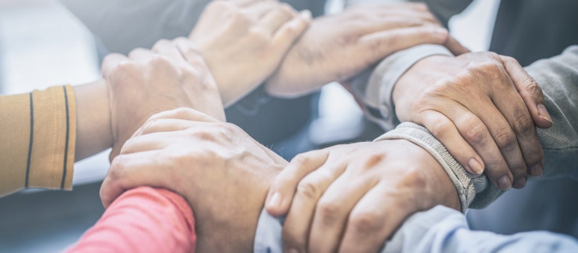 Dramatic moment. A group people hold strong hands. Sign of trust and teamwork. Corporate meeting concept.