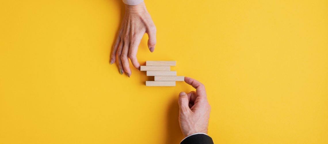 Hands of a businessman and businesswoman stacking wooden pegs in a conceptual image of business stability and teamwork.