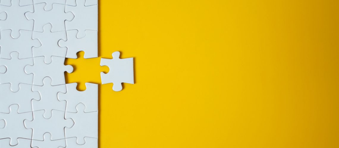 White jigsaw puzzle on yellow background. Team business success partnership or teamwork.