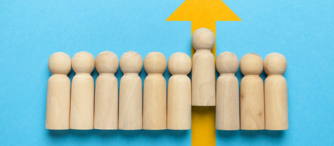 Wooden figures of people with a yellow arrow isolated on a blue background. Career and personal growth, business motivation.