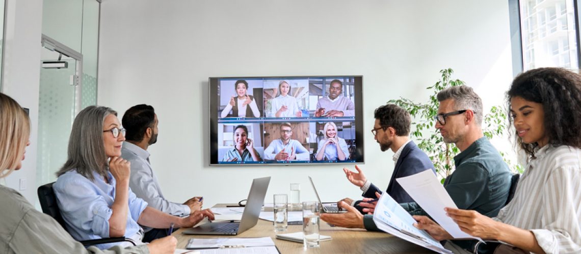 Diverse employees on online conference video call on tv screen in meeting room.