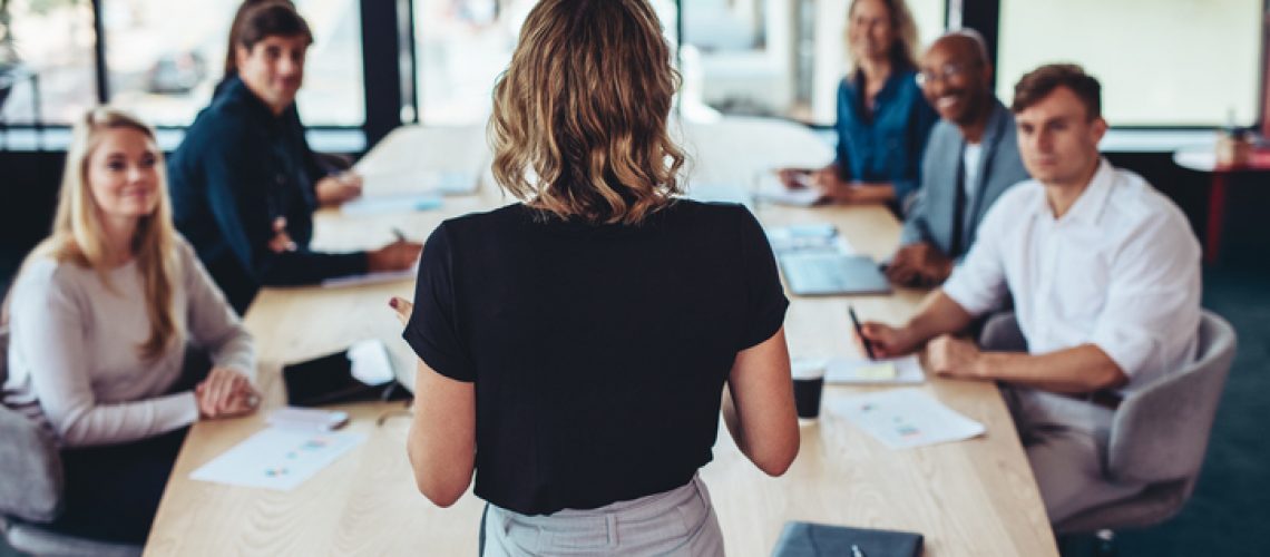 Rear view of a businesswoman addressing a meeting in office. Female manager having a meeting with her team in office boardroom.