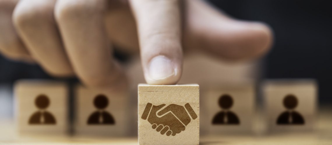 Hand putting hand shaking which print screen on wooden cube block  in front of human icon for business deal and agreement concept.