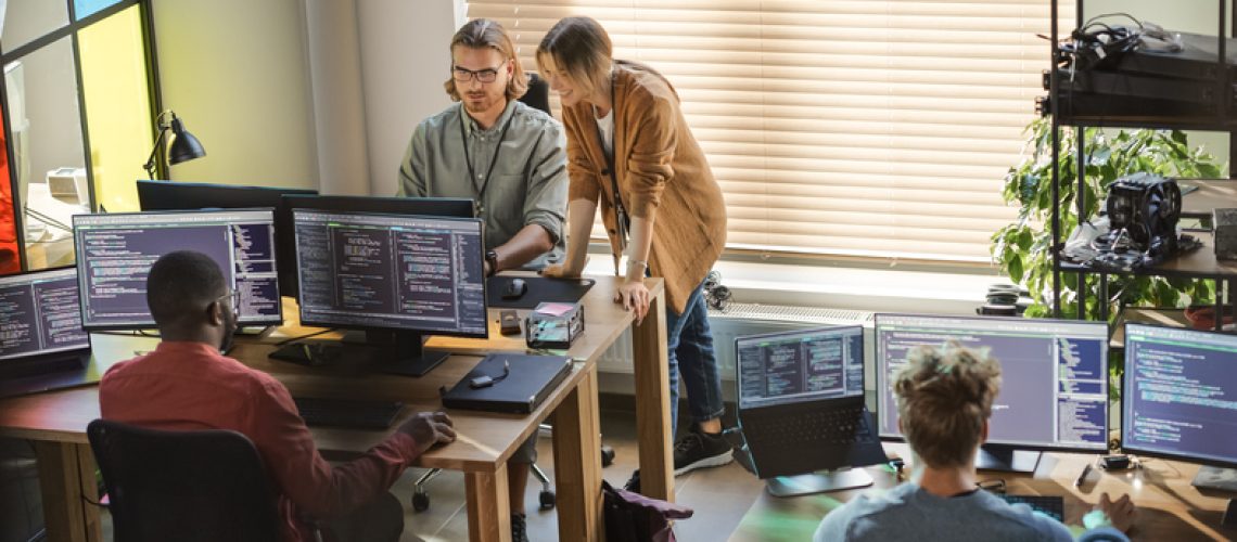 Creative Office: Diverse Colleagues Coding on Desktop Computers With Multiple Monitors. Female Project Manager Talks to Male Team Lead While Junior Developers Working on Mobile Application.