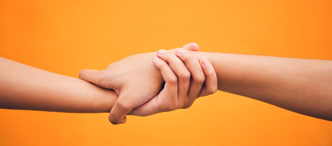 Holding hands, studio and closeup for support, help and care for teamwork by orange background. People, friends and together for solidarity, link and connection with synergy, partnership and strong