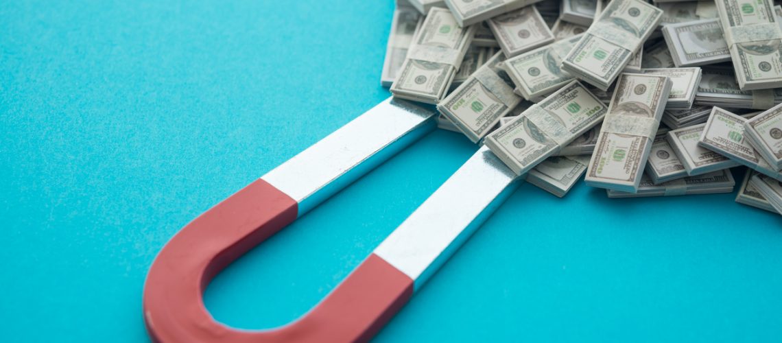 Horseshoe magnet attract heap US dollar bill banknotes on blue background. Concept of rich or wealth making money from retrun on investment (stock market, etf, mutual fund, etc.), new business, startup.