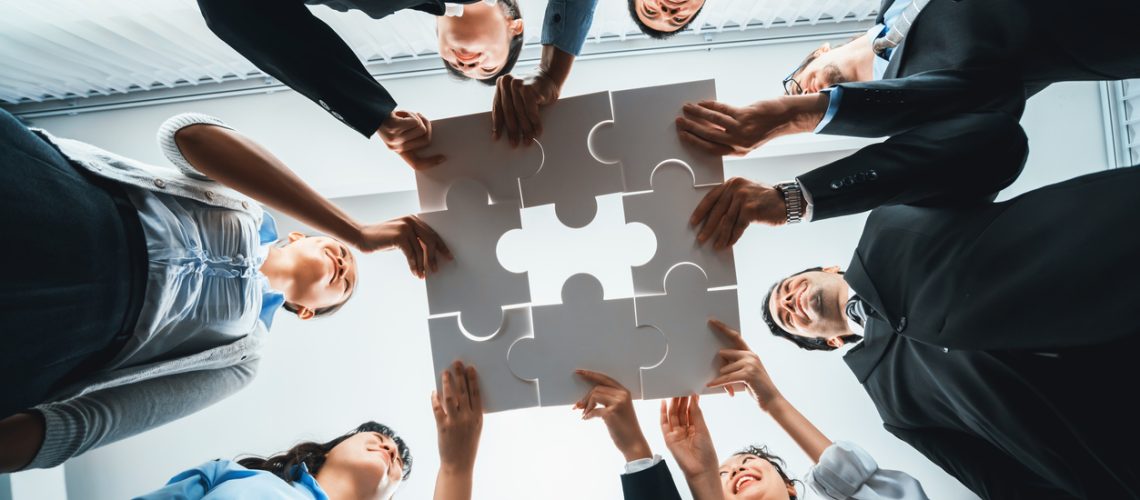 Multiethnic business people holding jigsaw pieces together. Habiliment Multiethnic business people holding jigsaw pieces and merge them together as effective solution solving teamwork, shared vision and common goal combining diverse talent. Below view. Habiliment