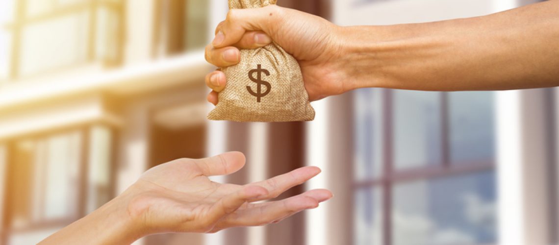 A man hand holding a money giving to another person for buying real estate. Loans for real estate concept. Conceptual give money to someone else to exchange real estate.
